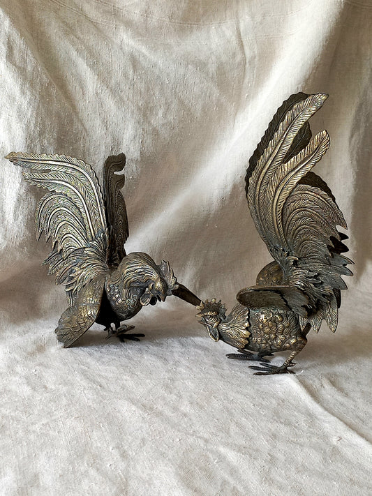 Two metallic rooster figurines on a textured white surface