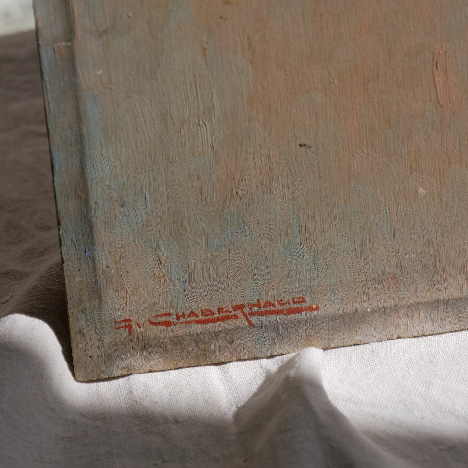 An original vintage oil painting depicting a village on the banks of a large river. It looks similar to the Rhine River Danube in Germany, and with the large hills/mountains in the background maybe the Black Forest, although it could be many places in Europe and perhaps even in France where we purchased this wonderful piece of original art on wooden board.