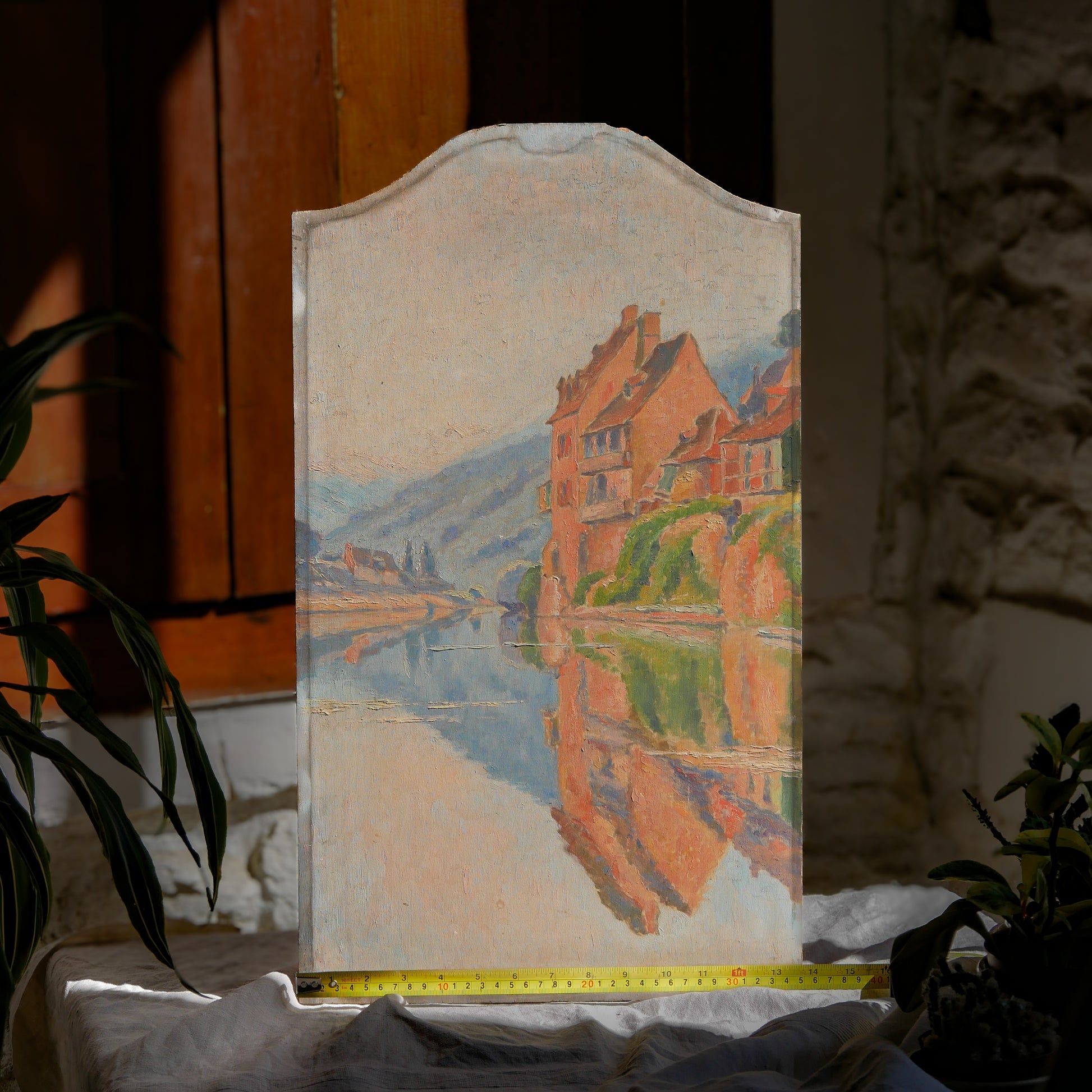 An original vintage oil painting depicting a village on the banks of a large river. It looks similar to the Rhine River Danube in Germany, and with the large hills/mountains in the background maybe the Black Forest, although it could be many places in Europe and perhaps even in France where we purchased this wonderful piece of original art on wooden board.
