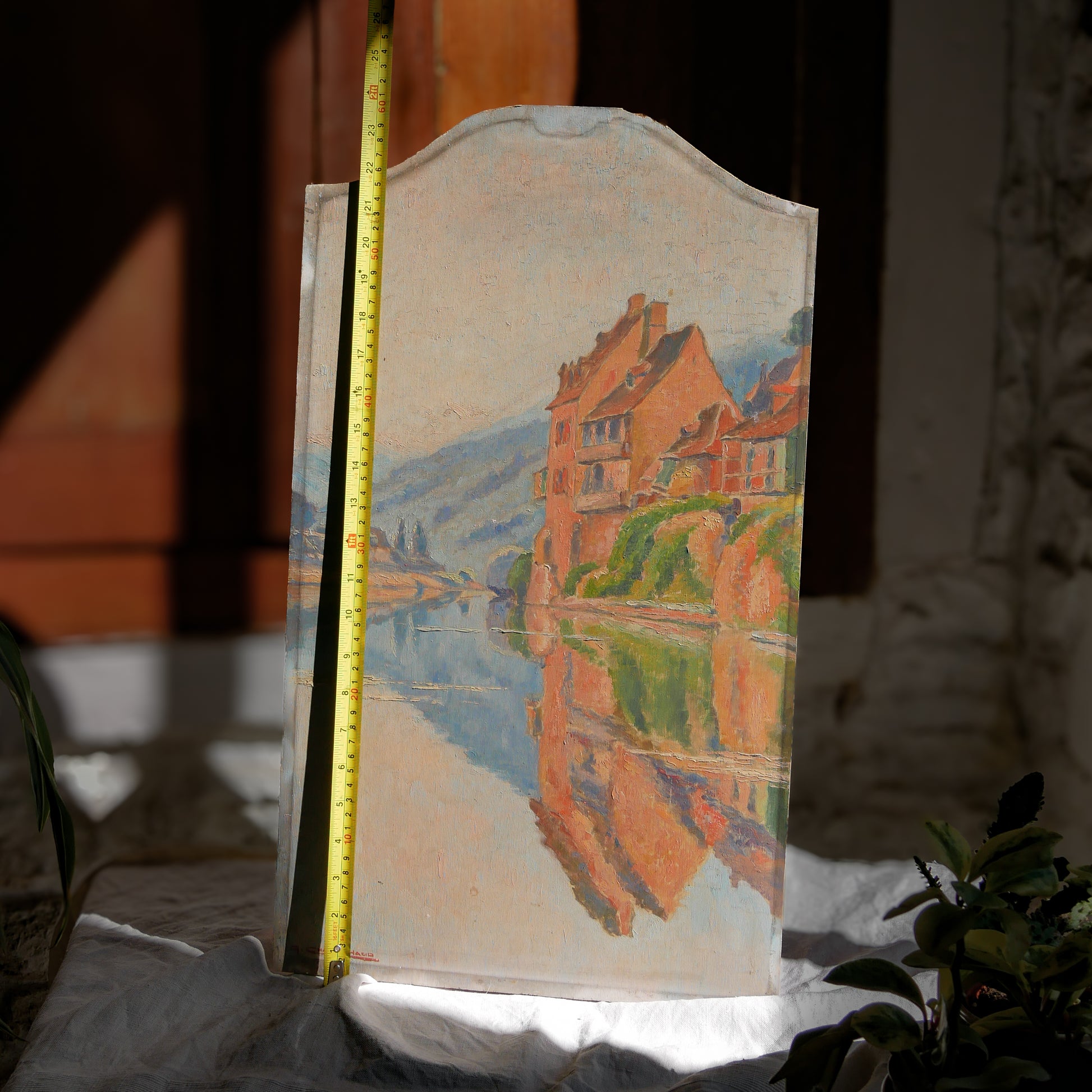 An original vintage oil painting depicting a village on the banks of a large river. It looks similar to the Rhine River Danube in Germany, and with the large hills/mountains in the background maybe the Black Forest, although it could be many places in Europe and perhaps even in France where we purchased this wonderful piece of original art on wooden board.