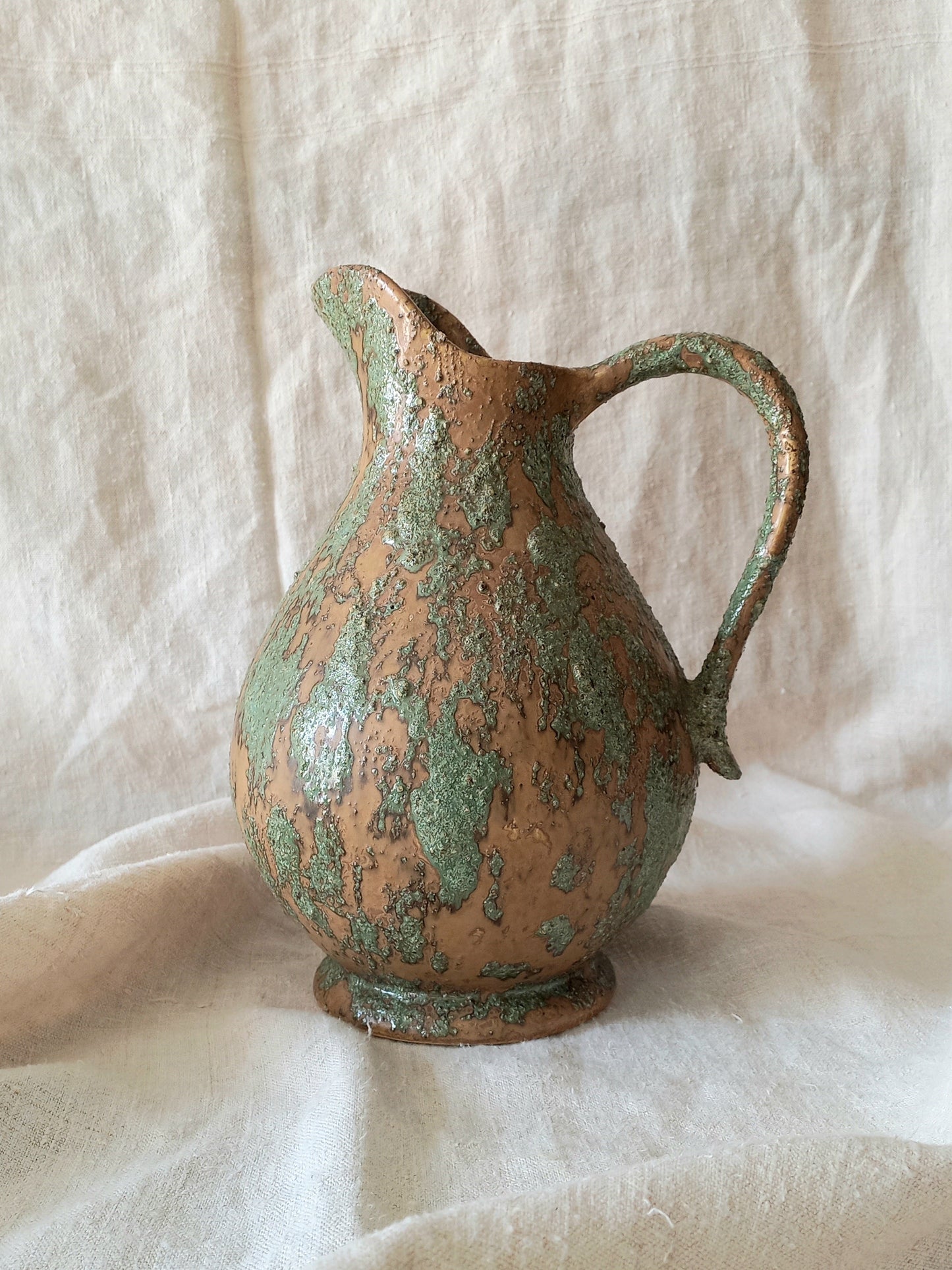 Large artisan made vintage pottery jug with green and earth tones on a beige background