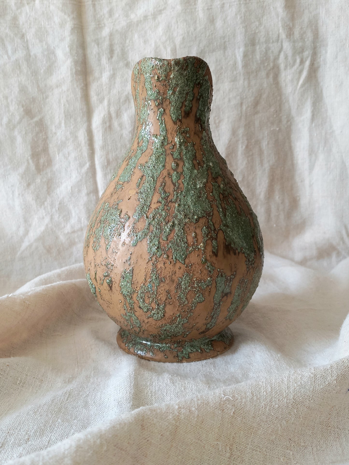Ceramic vase with green glaze on a textured white background