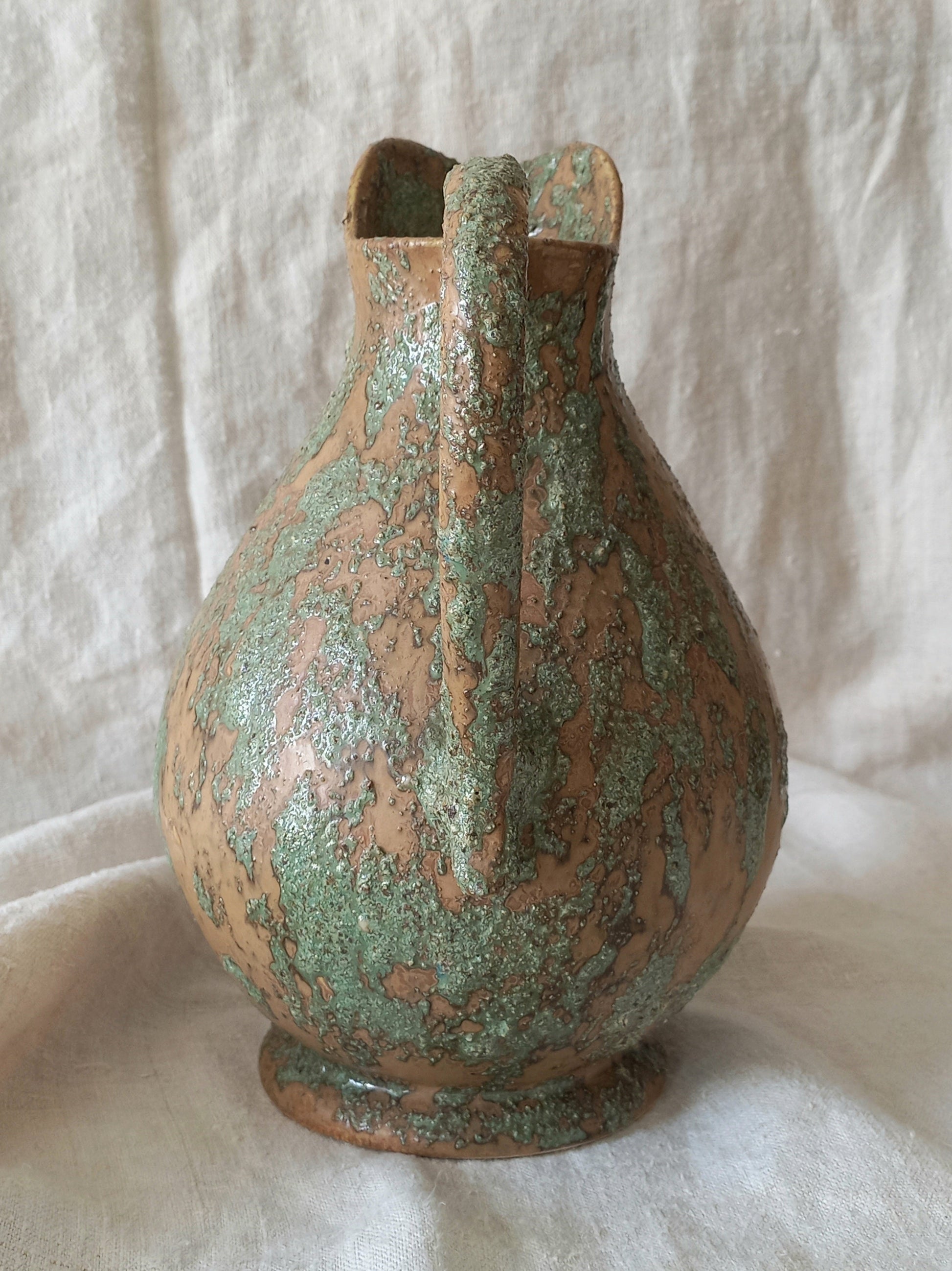 Large artisan made vintage pottery jug with green and earth tones on a beige background