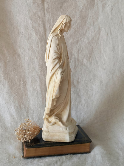 Statue of a draped figure on a Bible against a textured beige background