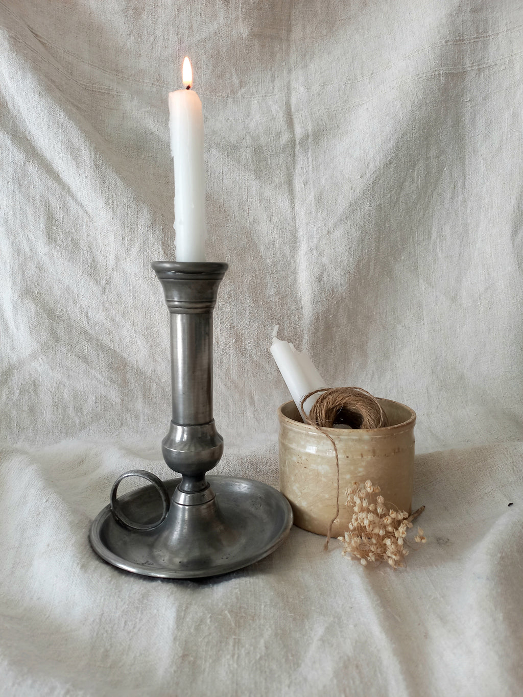 pewter candlestick holder with a lit candle on a textured white fabric background