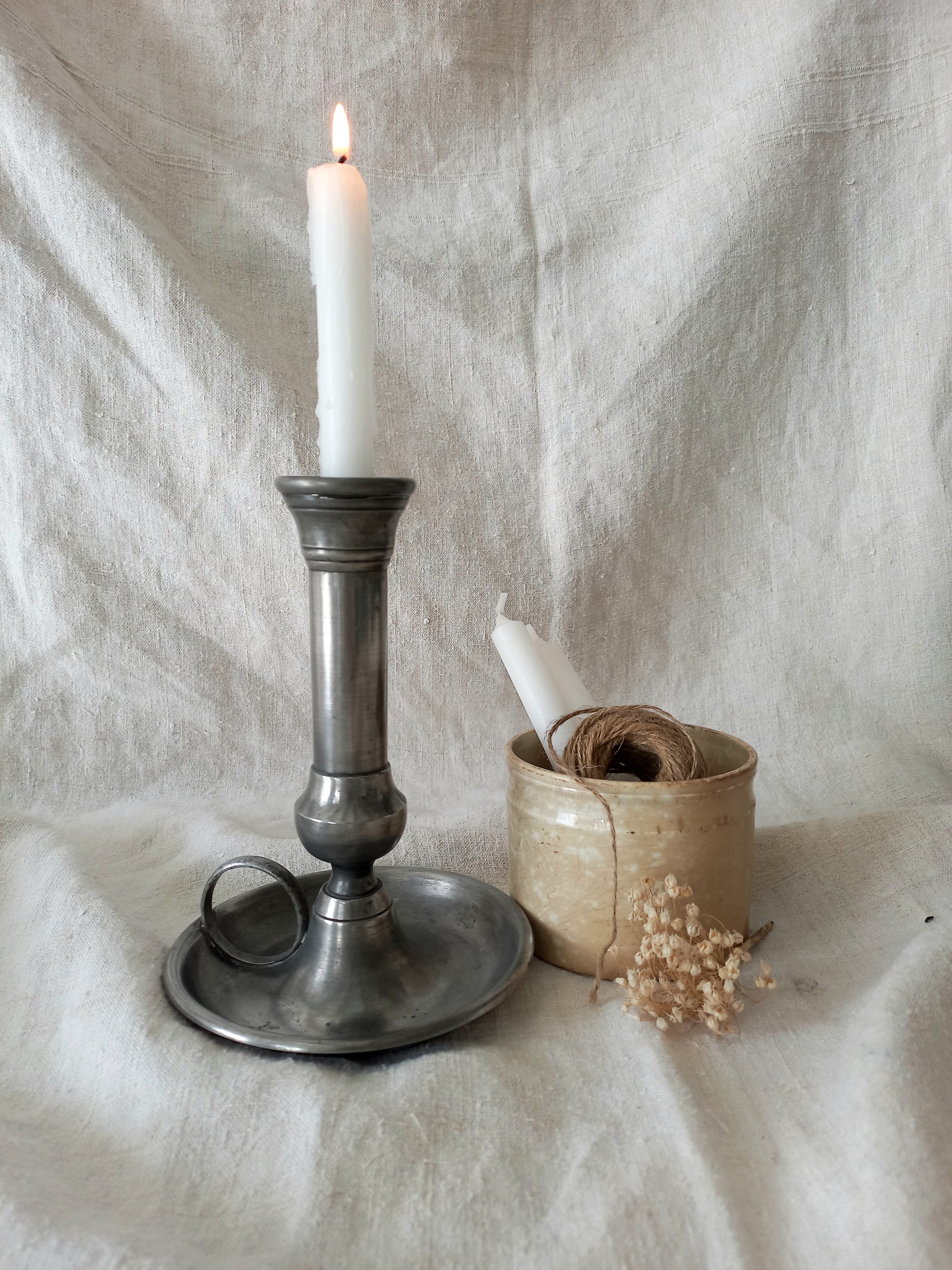 pewter candlestick holder with a lit candle on a textured white fabric background