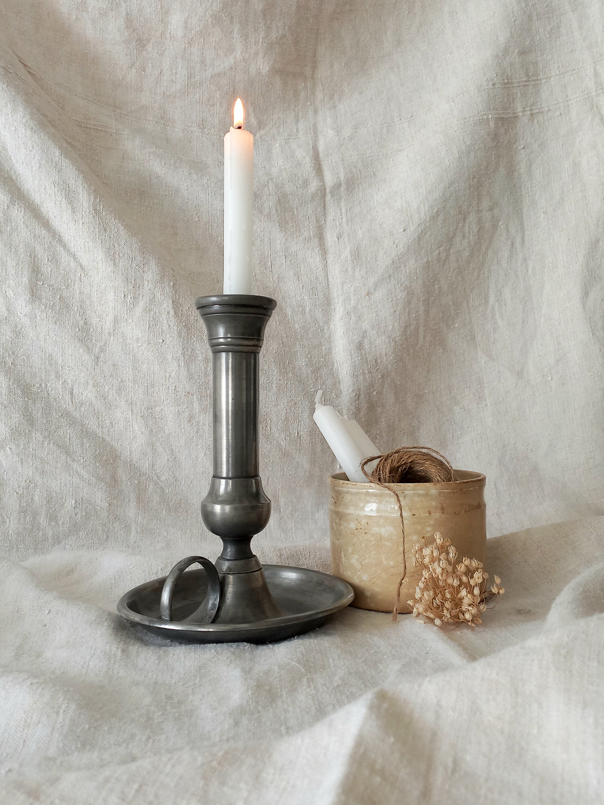 pewter candlestick holder with a lit candle on a textured white fabric background