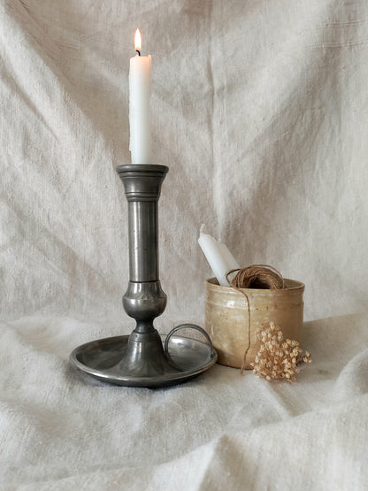 pewter candlestick holder with a lit candle on a textured white fabric background